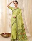 Woman wearing a light green saree with a floral border against a beige curtain background