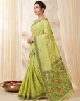 Woman wearing a light green saree with a floral border against a beige curtain background