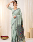 Woman wearing a light blue saree with floral patterns against a white curtain background