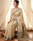 Woman wearing a traditional beige saree with floral patterns in a bright room.
