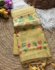 Yellow fabric with floral patterns on a textured surface with flowers and a basket in the background.