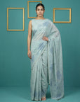 Woman wearing a light blue saree with a subtle pattern against a teal background