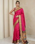 Woman wearing a pink saree with gold border against a beige curtain background