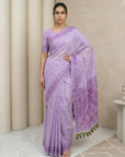 Woman wearing a light purple saree with a patterned border indoors.