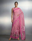 Woman wearing a pink saree with a white blouse against a gray background
