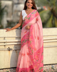 Woman wearing a pink saree with floral patterns outdoors.