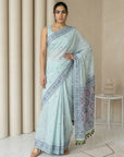 Woman wearing a light blue saree with a patterned border in a minimalistic setting.