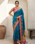 Woman wearing a blue saree with a pink border in an indoor setting.