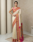 Woman wearing a cream saree with pink and orange border in a minimalistic setting
