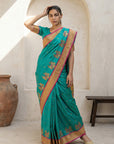 Woman wearing a green saree with gold border in an indoor setting