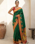Woman wearing a green and orange saree in a room with a white wall and wooden bench.