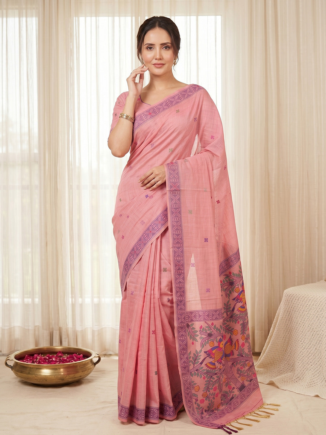 Woman wearing a pink saree with a decorative border in a well-lit room.