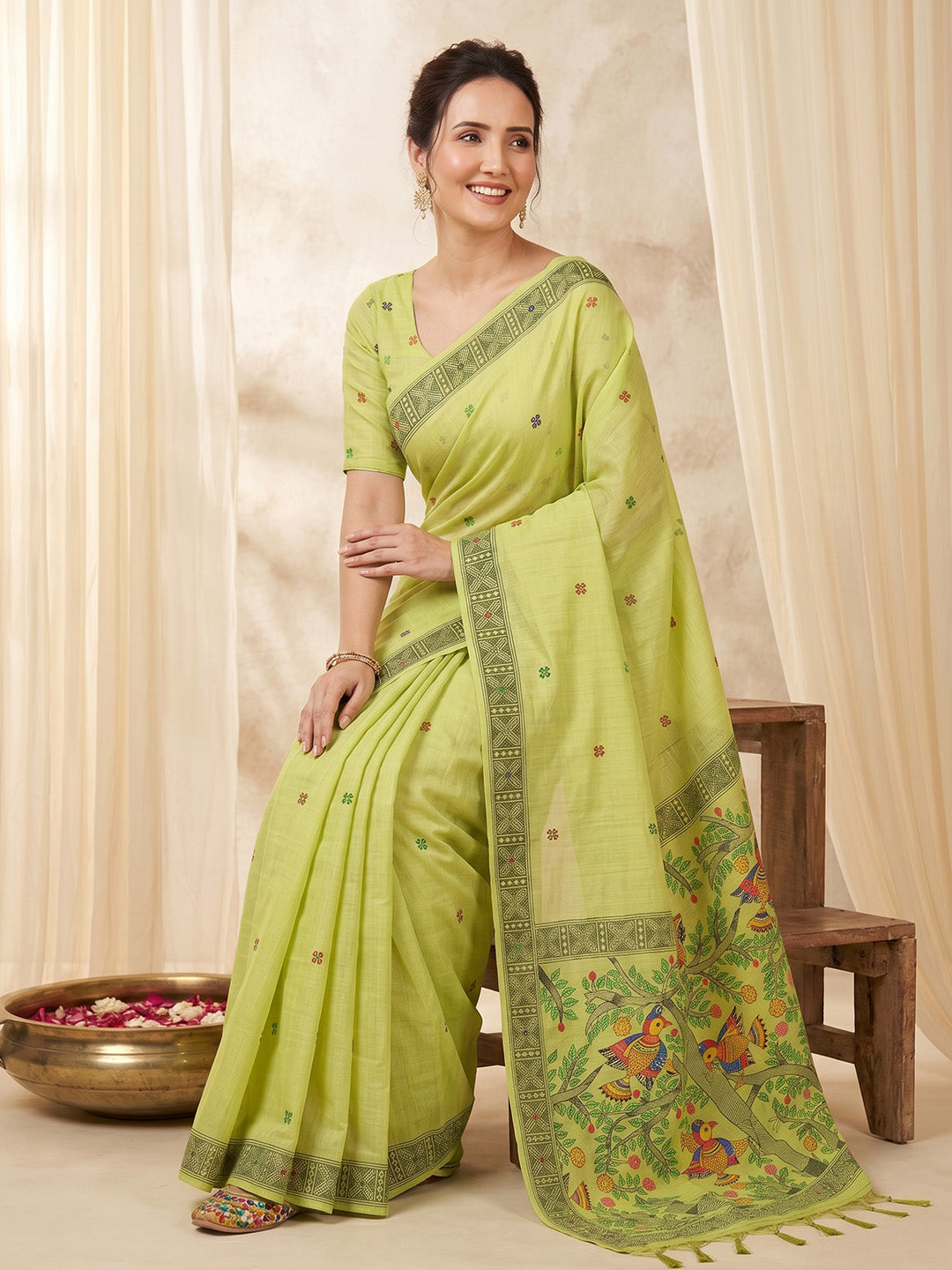 Woman wearing a green saree with a floral pattern against a beige curtain background