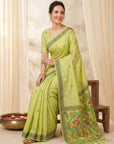 Woman wearing a green saree with a floral pattern against a beige curtain background