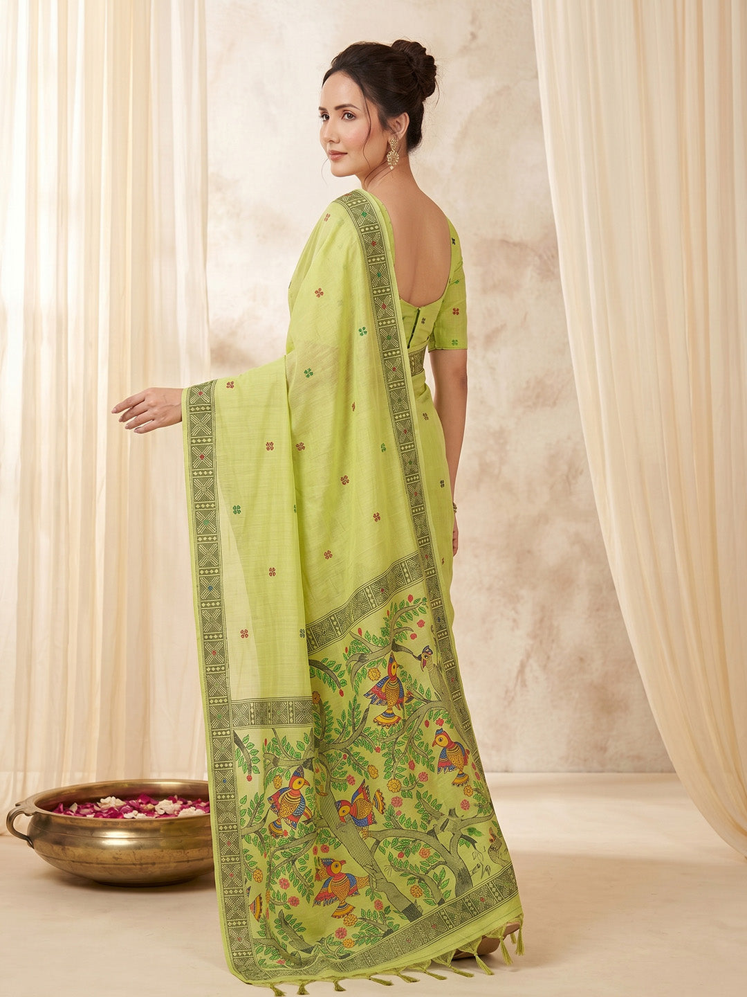 Woman wearing a green saree with intricate patterns in a neutral setting