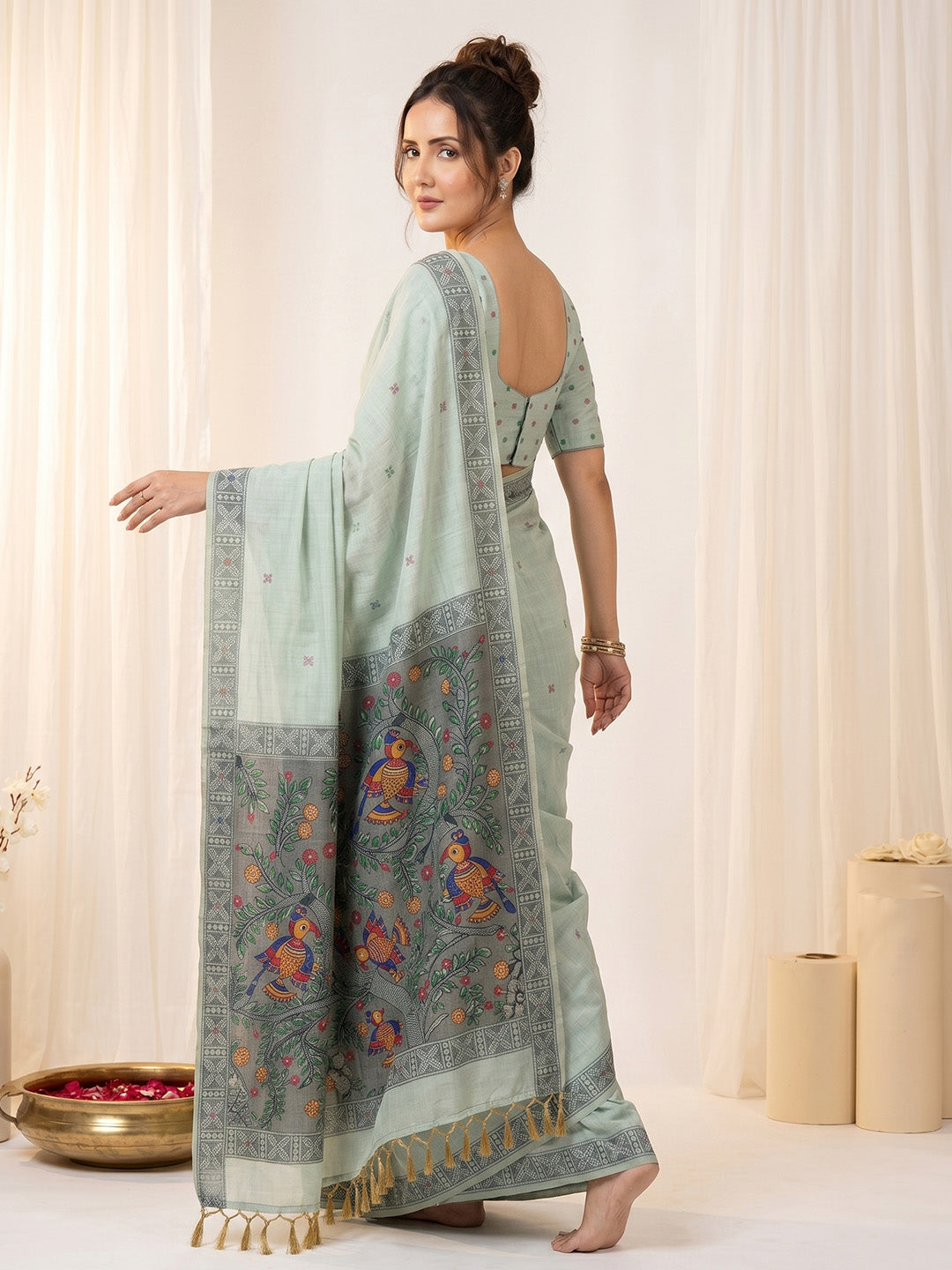 Woman wearing a light blue saree with a pattern, standing against a white curtain background.