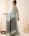 Woman wearing a light blue saree with a pattern, standing against a white curtain background.