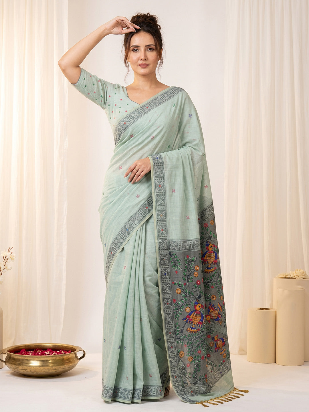 Woman wearing a light blue saree with floral patterns against a white curtain background