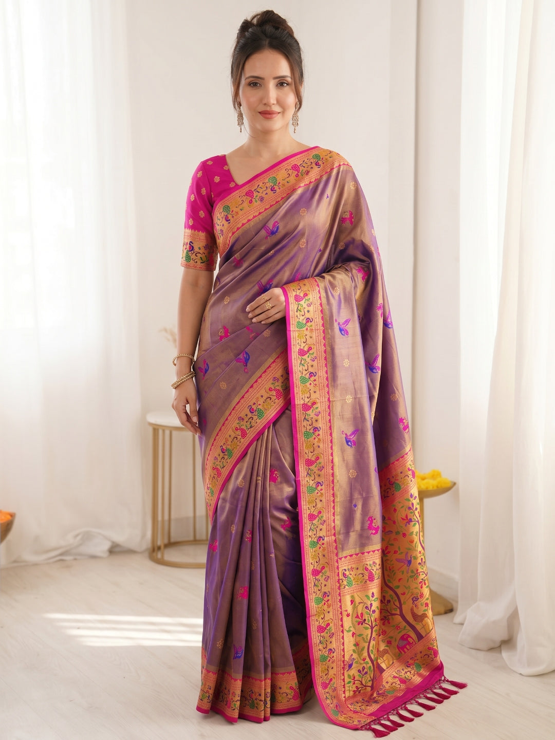 Woman wearing a traditional saree with a purple and pink design in a minimalistic setting.