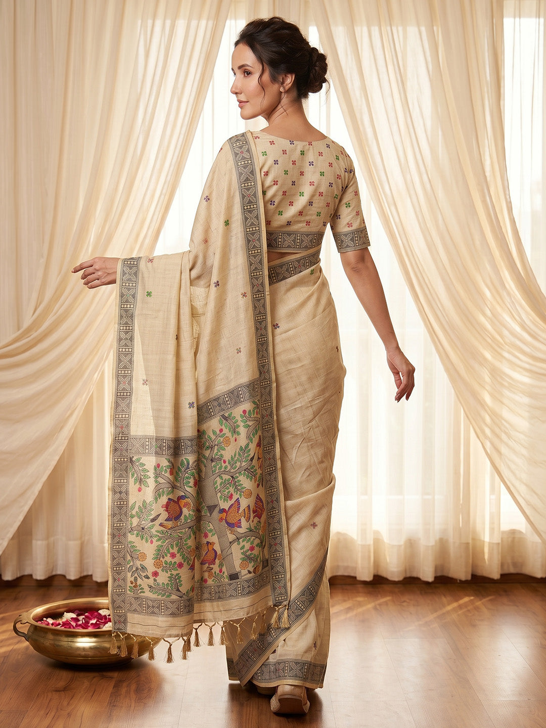 Woman wearing a traditional saree with a floral pattern in a room with white curtains.