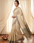 Woman wearing a beige saree with floral patterns in front of white curtains.
