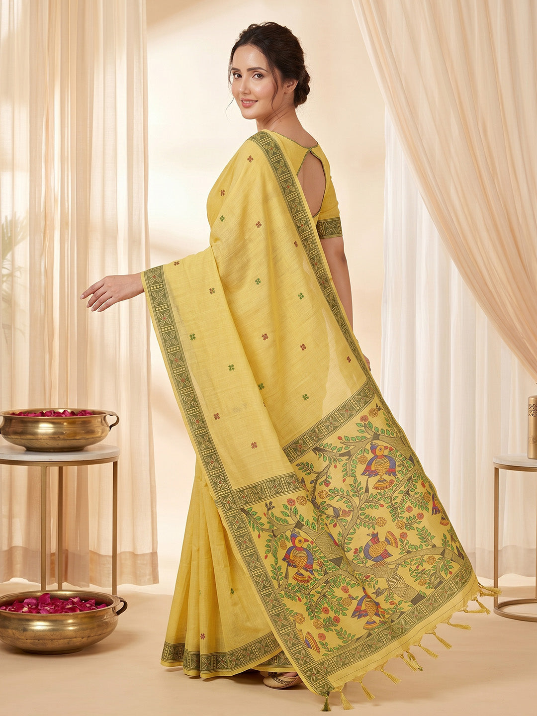 Woman wearing a yellow saree with intricate patterns in a softly lit room.