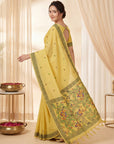 Woman wearing a yellow saree with intricate patterns in a softly lit room.
