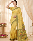 Woman wearing a yellow saree with intricate patterns in a softly lit room.