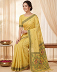 Woman wearing a yellow saree with a decorative border, sitting in a well-lit room.