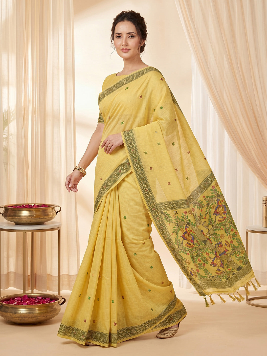 Woman wearing a yellow saree with a decorative border in a softly lit room.