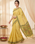 Woman wearing a yellow saree with a decorative border in a softly lit room.