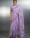 Woman wearing a lavender saree with a floral pattern on a gray background