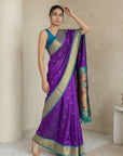 Woman wearing a purple saree with a blue blouse in a minimal indoor setting