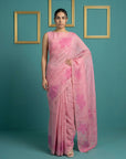 Woman wearing a pink saree with floral patterns against a teal background