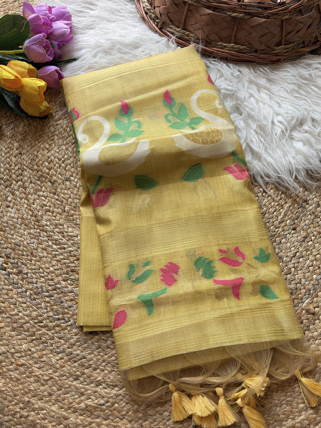 Yellow fabric with floral patterns on a textured surface with flowers and a basket in the background.