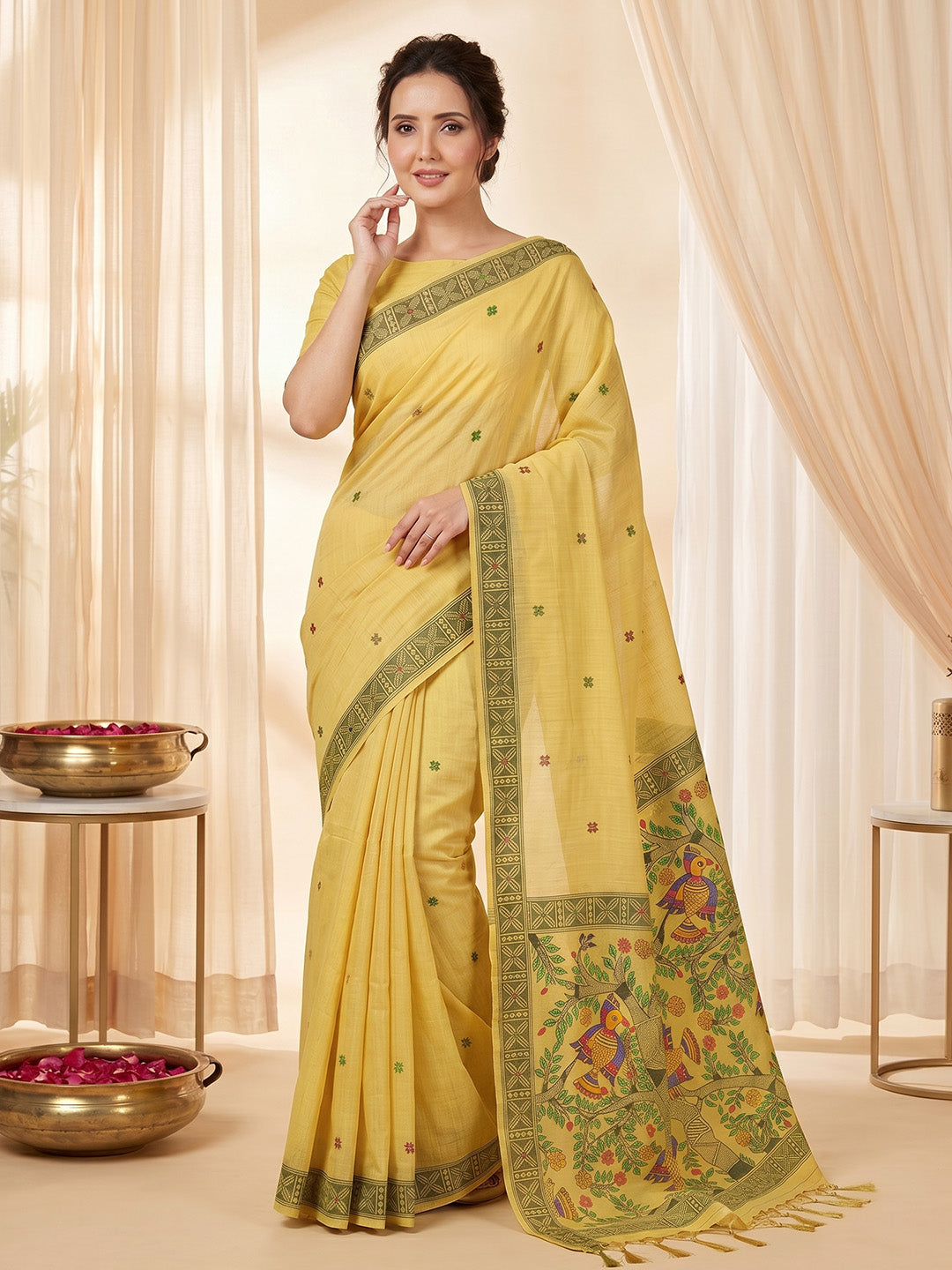 Woman wearing a yellow saree with intricate patterns in a softly lit room.