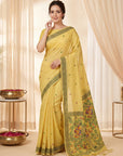 Woman wearing a yellow saree with intricate patterns in a softly lit room.