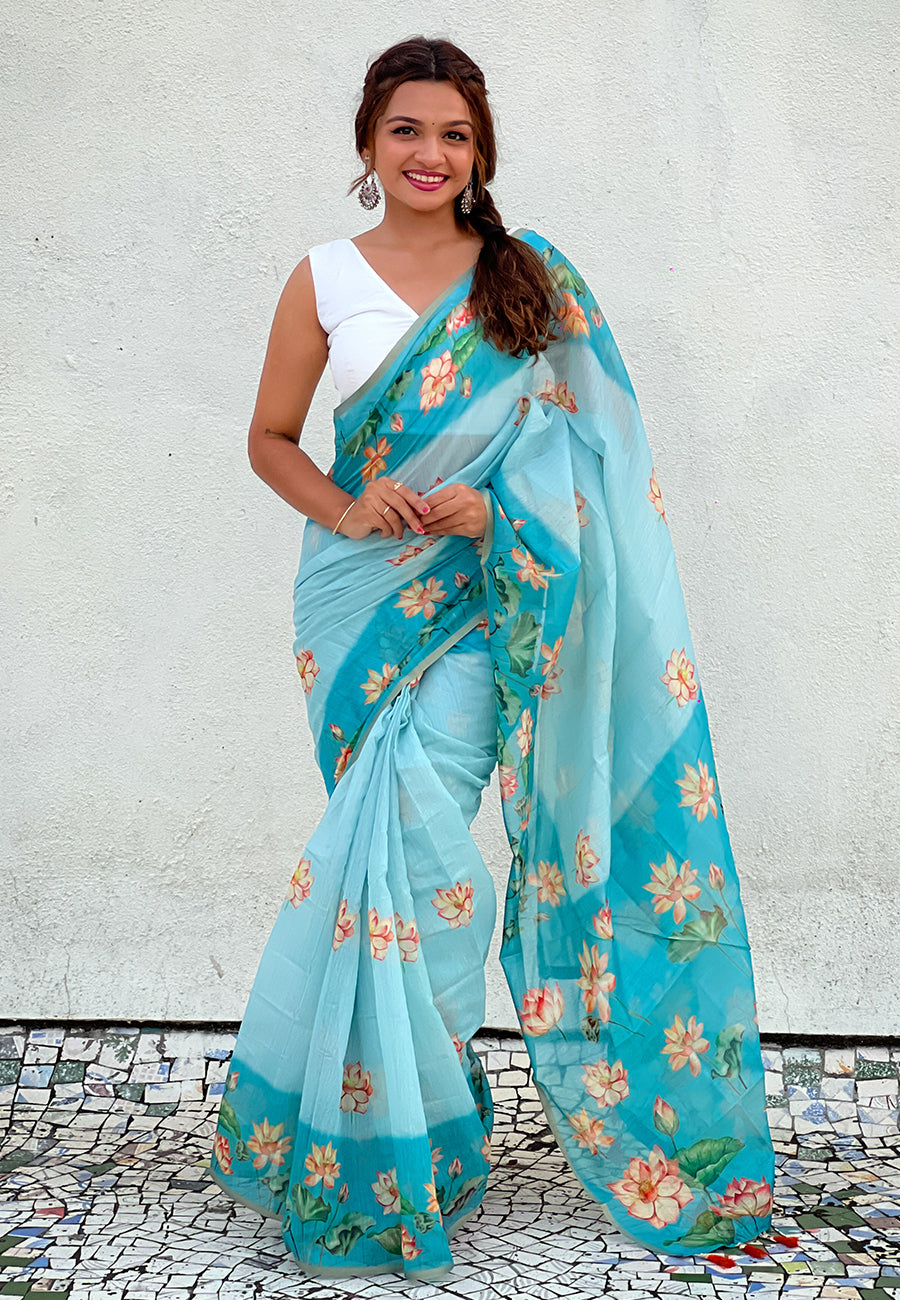 Woman wearing a light blue saree with floral patterns against a white wall.