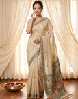 Woman wearing a beige saree with floral patterns in a room with white curtains.