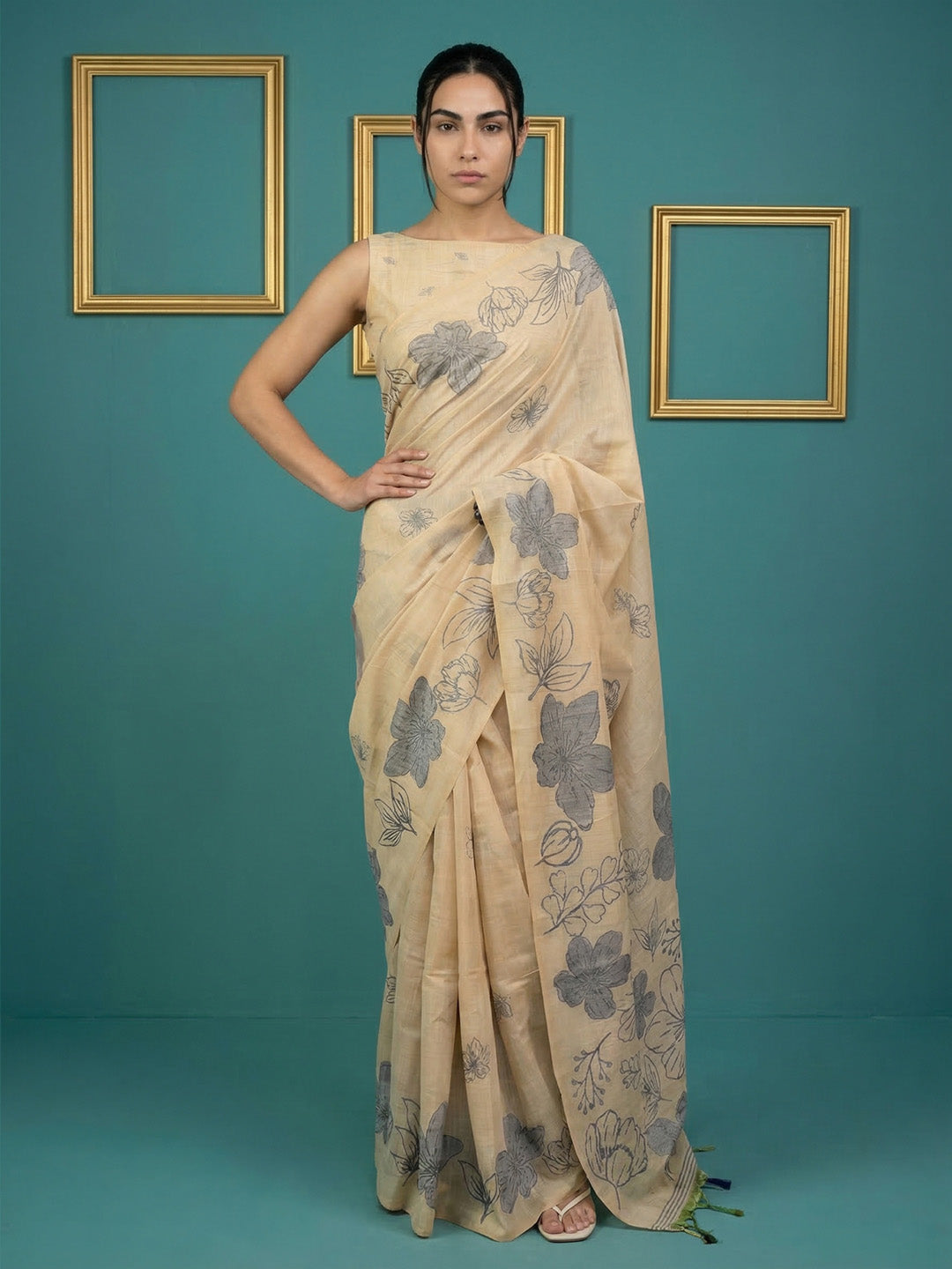 Woman wearing a beige saree with floral patterns against a teal background