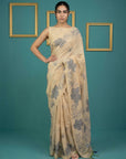 Woman wearing a beige saree with floral patterns against a teal background
