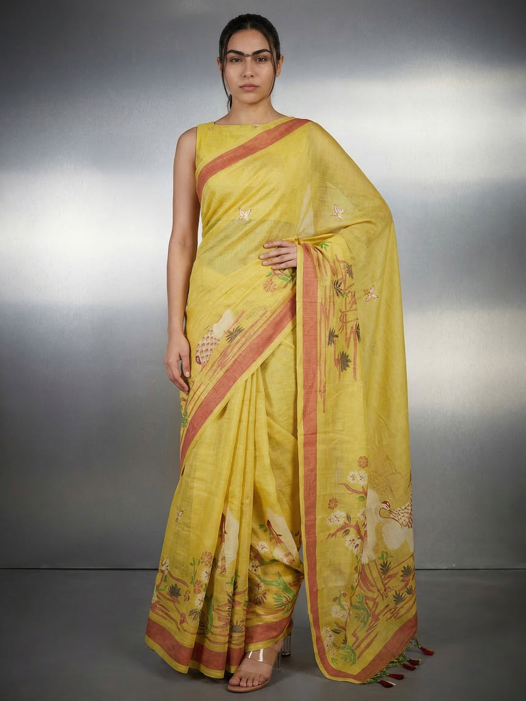 Woman wearing a yellow saree with a red border against a gray background