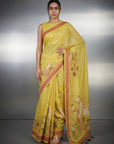 Woman wearing a yellow saree with a red border against a gray background