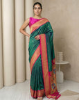 Woman wearing a green and pink saree in a room with beige curtains and a white table.