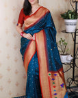 Woman wearing a blue saree with a pattern, standing indoors.