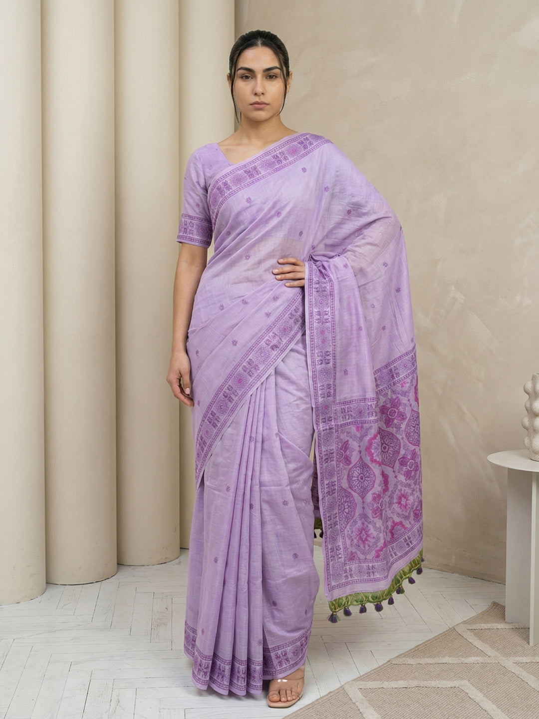 Woman wearing a light purple saree with a patterned border indoors.