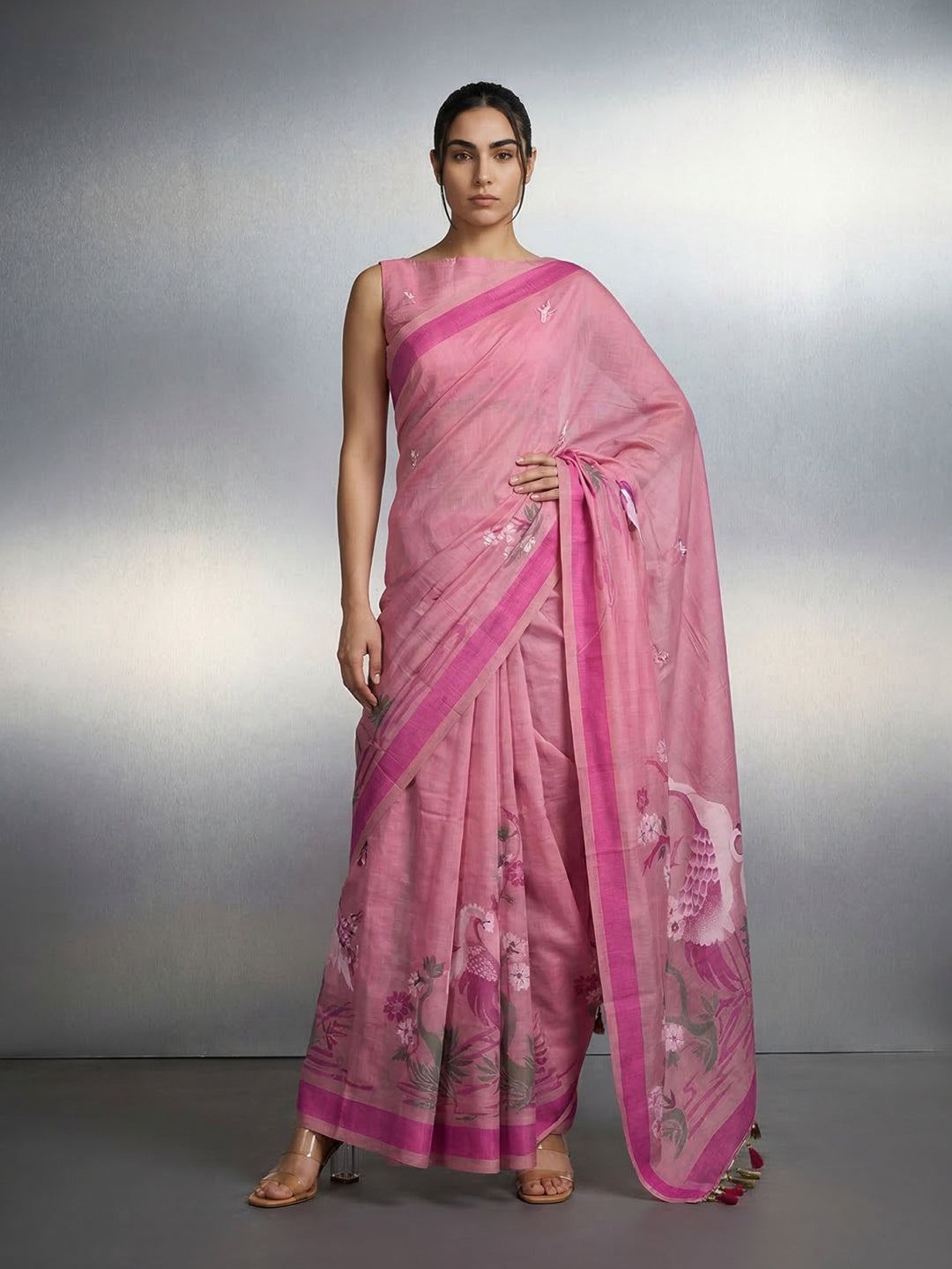 Woman wearing a pink saree with a white blouse against a gray background
