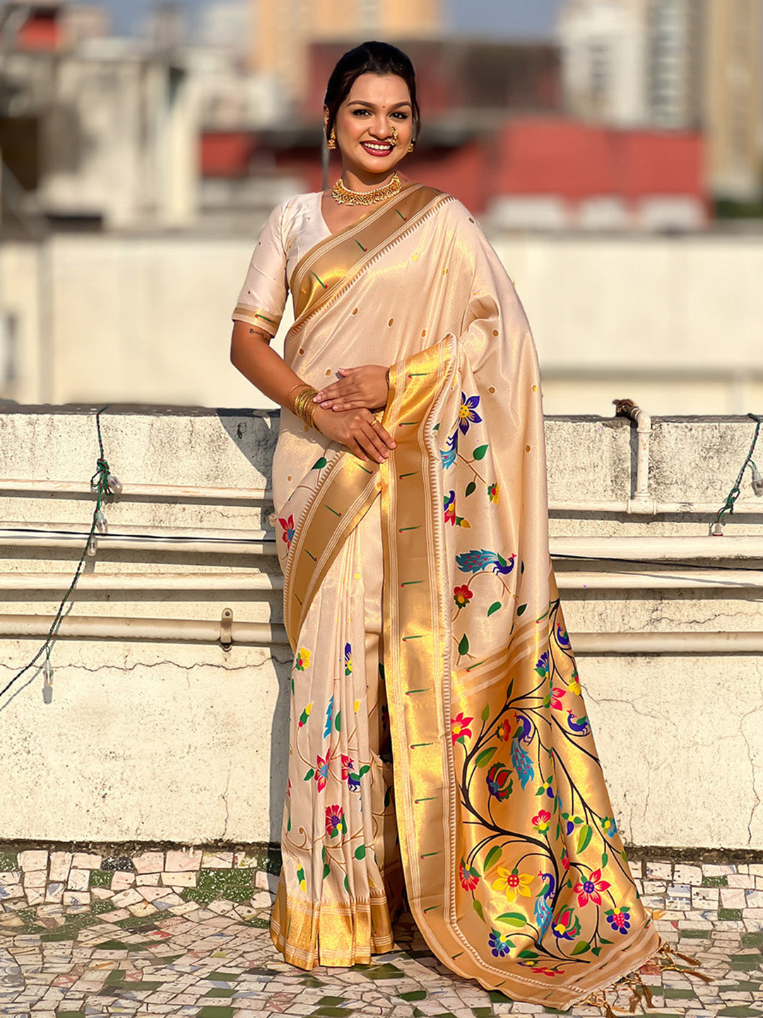 Woman in a beige saree with floral patterns standing on a rooftop.