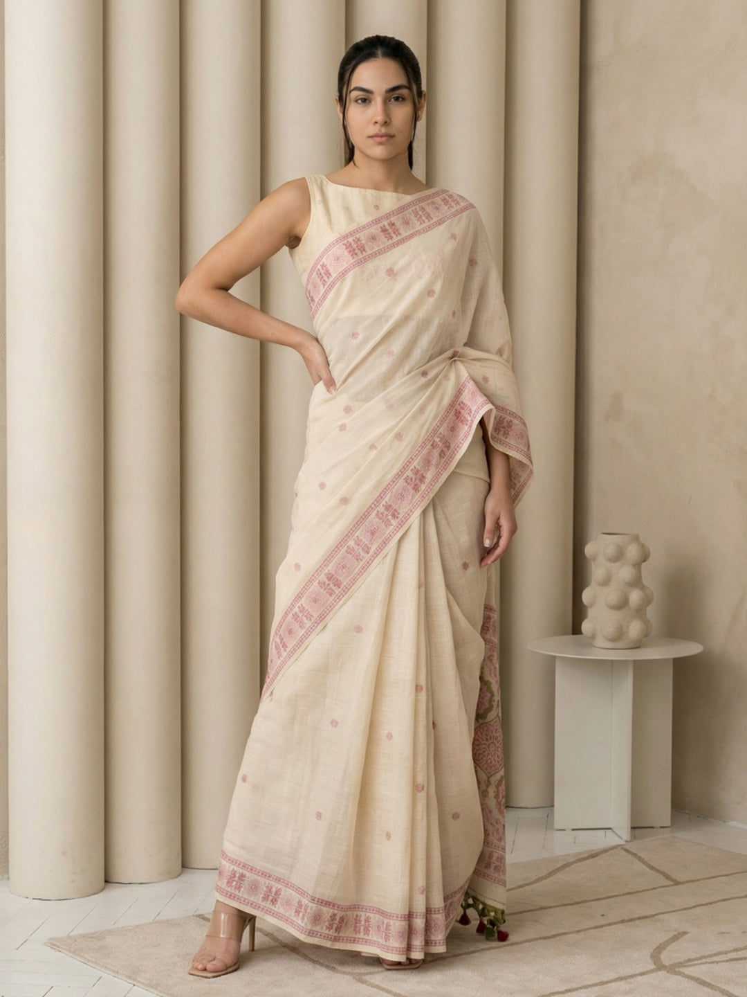 Woman wearing a beige saree with pink border in a minimalistic room.