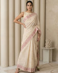 Woman wearing a beige saree with pink border in a minimalistic room.
